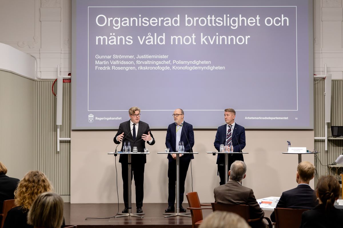Three persons are standing on a stage holding speeches.