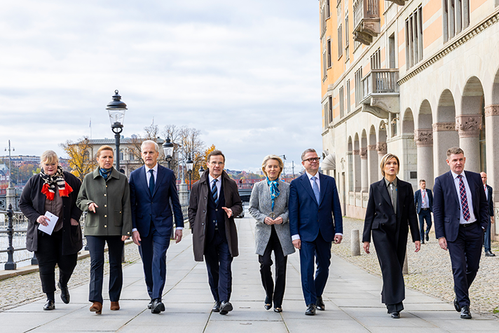Katrin Sjögren, Mette Fredriksen, Jonas Gahr Støre, Ulf Kristersson, Ursula von der Leyen, Petteri Orpo, Kristrún Frostadóttir och Aksel V. Johannesen walking side by side along Strömgatan in Stockholm. Rosenbad is visible in the background.