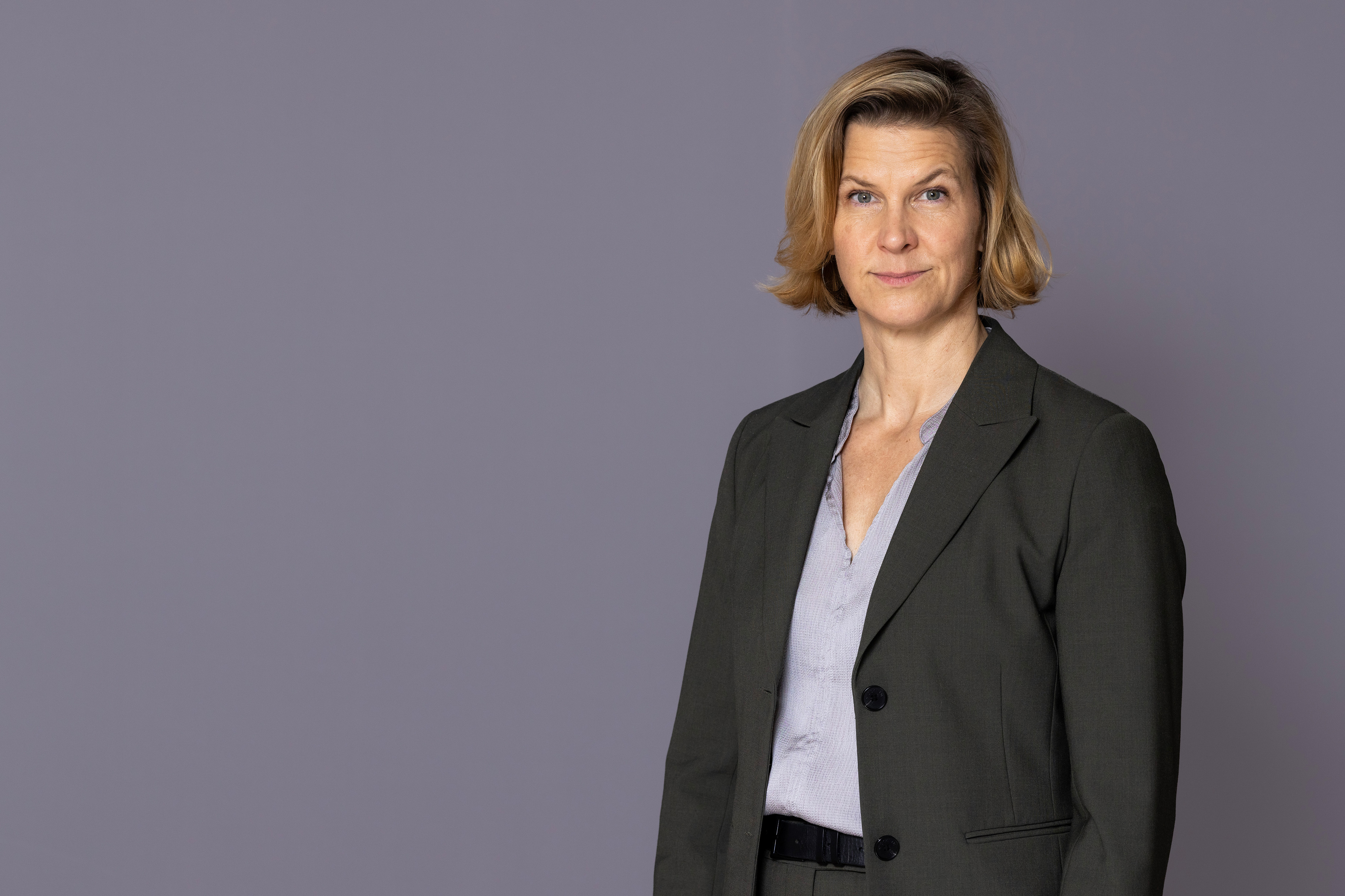 Minister for Gender Equality Nina Larsson stands in front of a gray wall and looks into the camera.