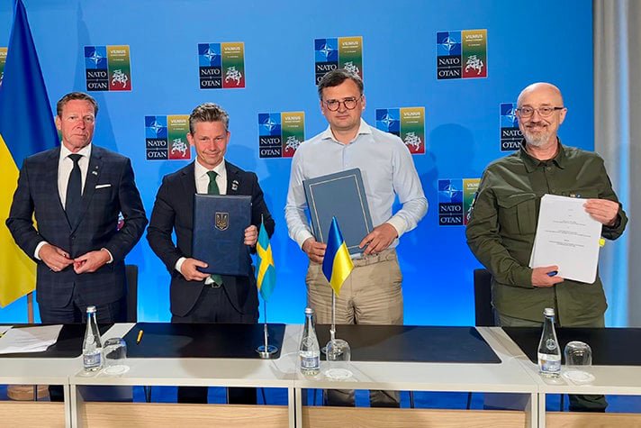 Four men stands next to each other. In the background you can see the logotype of Nato and the logotype of Vilnius, capital of Lithuania.