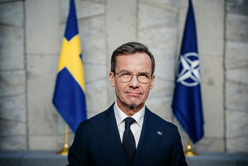 Kristersson standing in front of the Swedisf flag and the NATO flag.