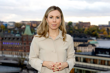EU-ministern tittar in i kameran. I bakgrunden syns en del av Riddarholmen och Södermalm i Stockholm.
